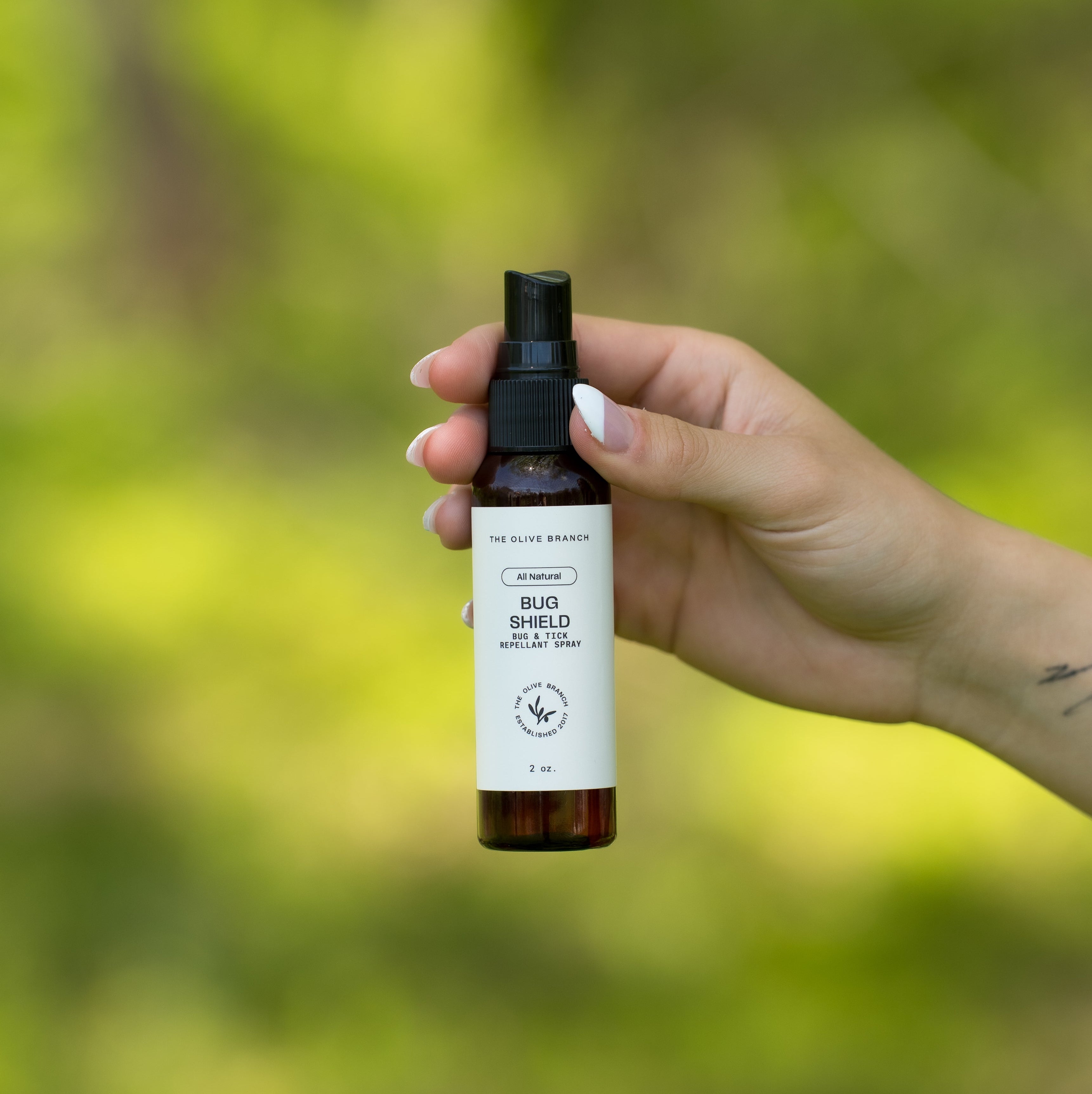 Hand holding a bottle with a label against a blurred green natural background