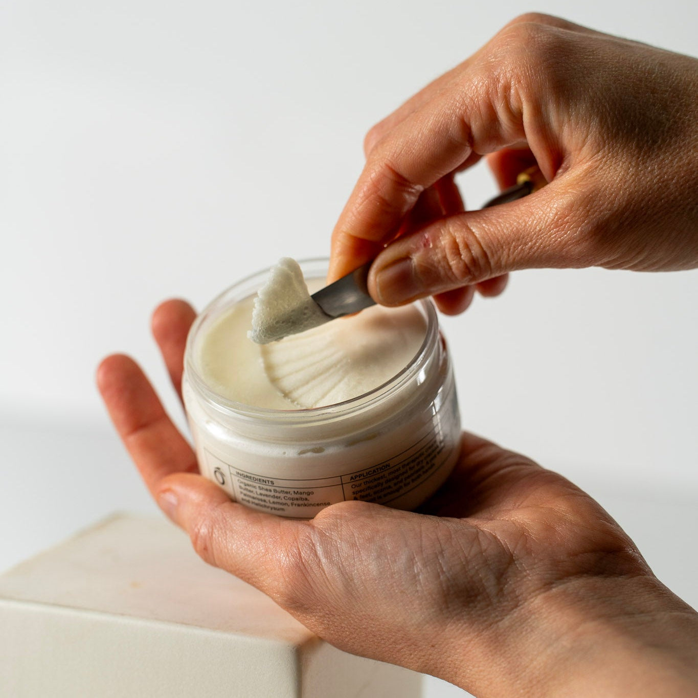 Hand scooping ultra thick signature cream from a jar with a spoon on a light background
