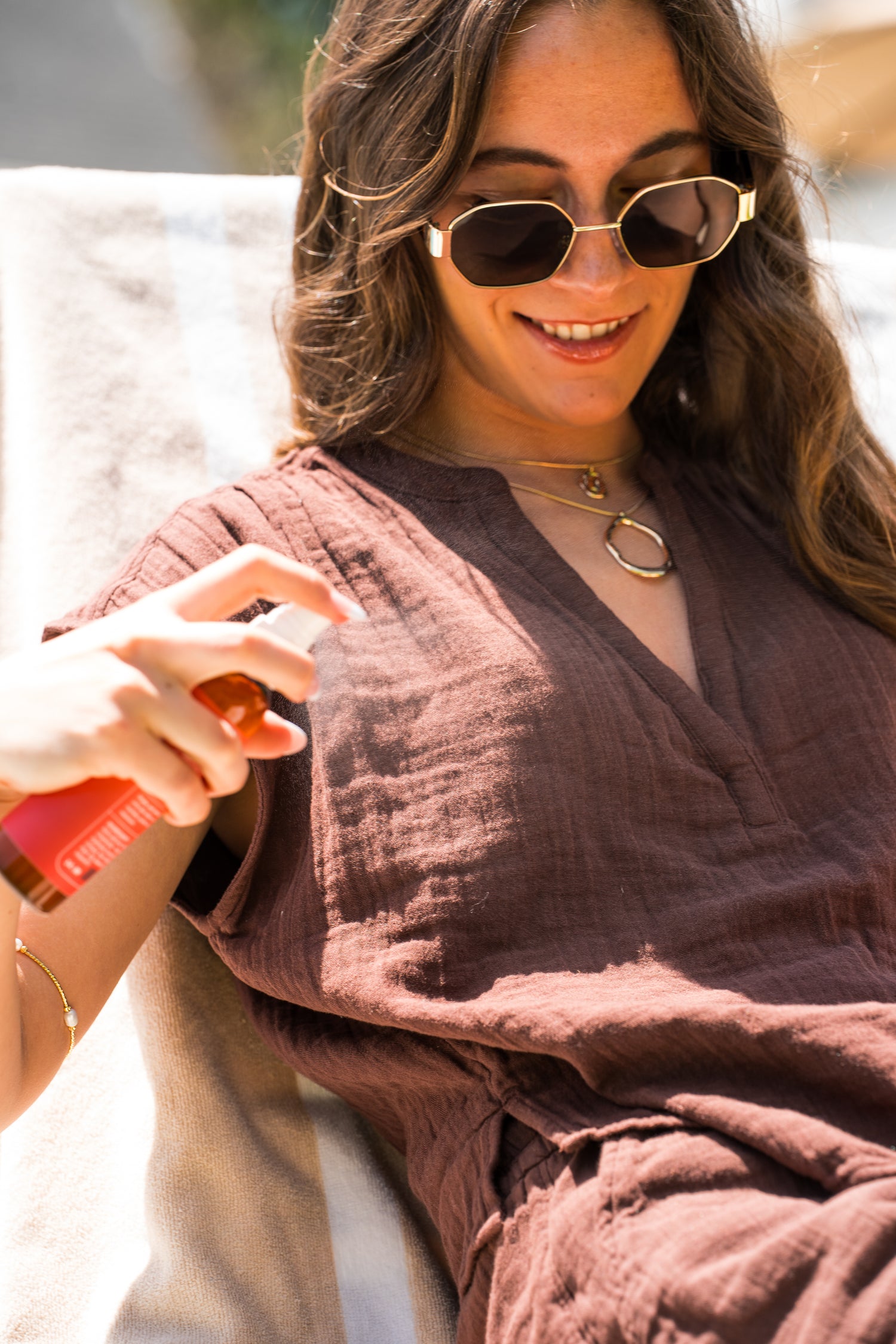 Woman wearing sunglasses and a brown robe, holding a red object.