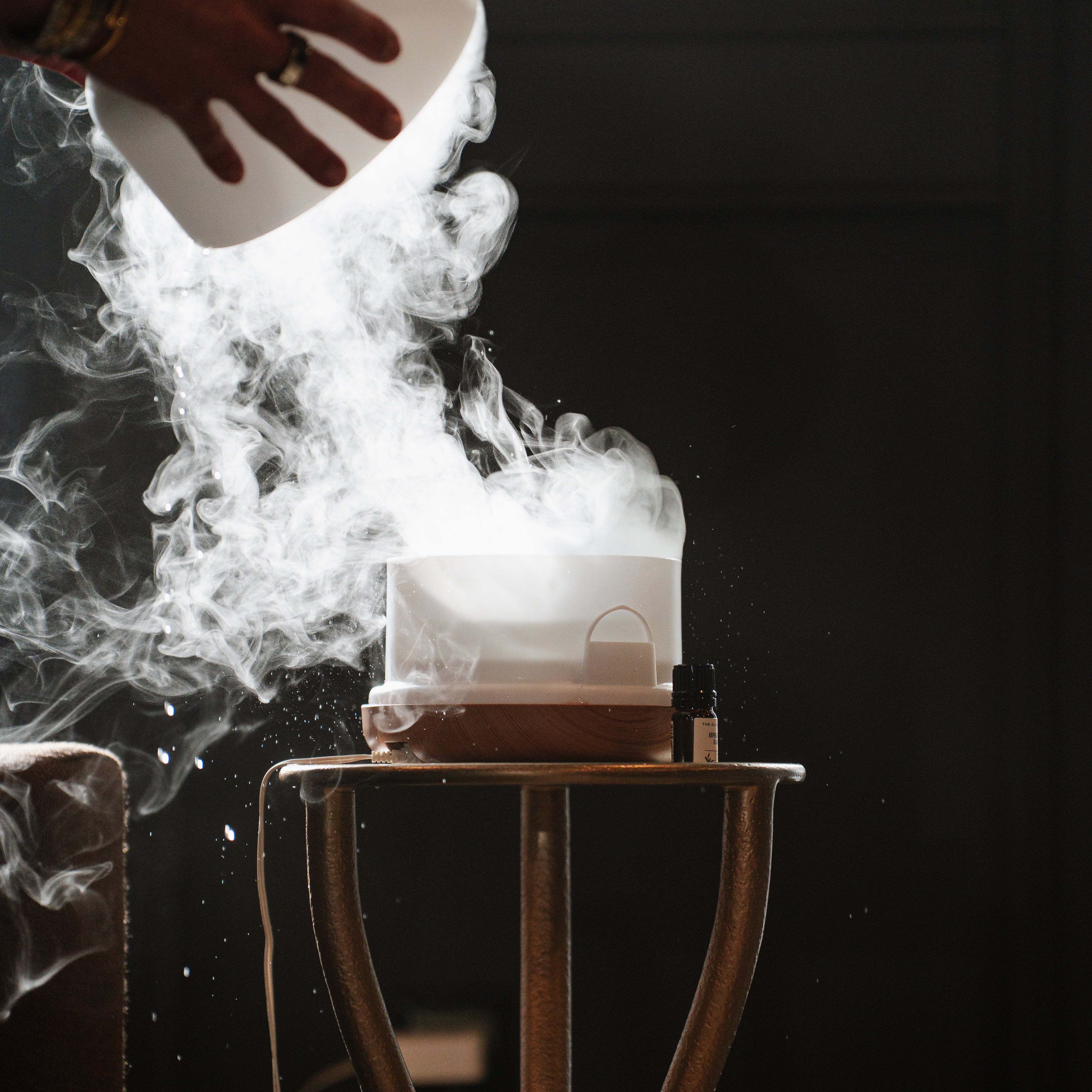 Oil diffuser emitting smoke on a dark background