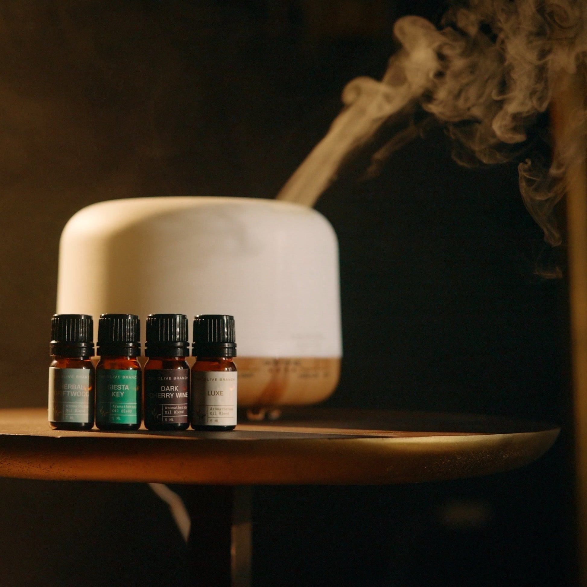 Essential oil bottles on a wooden table with a diffuser and smoke in the background