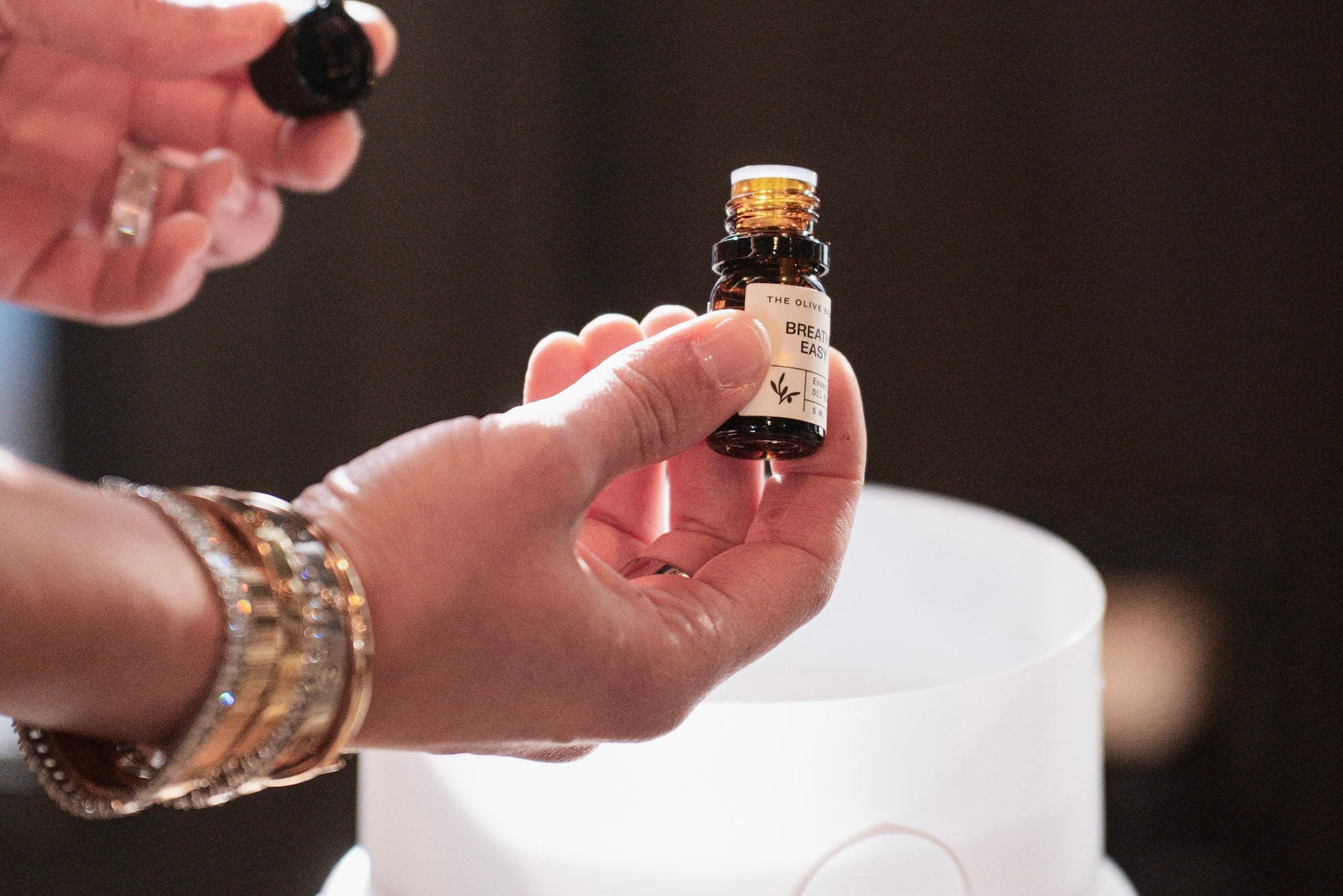 Person holding a small bottle of essential oil above an ultrasonic humidifier.