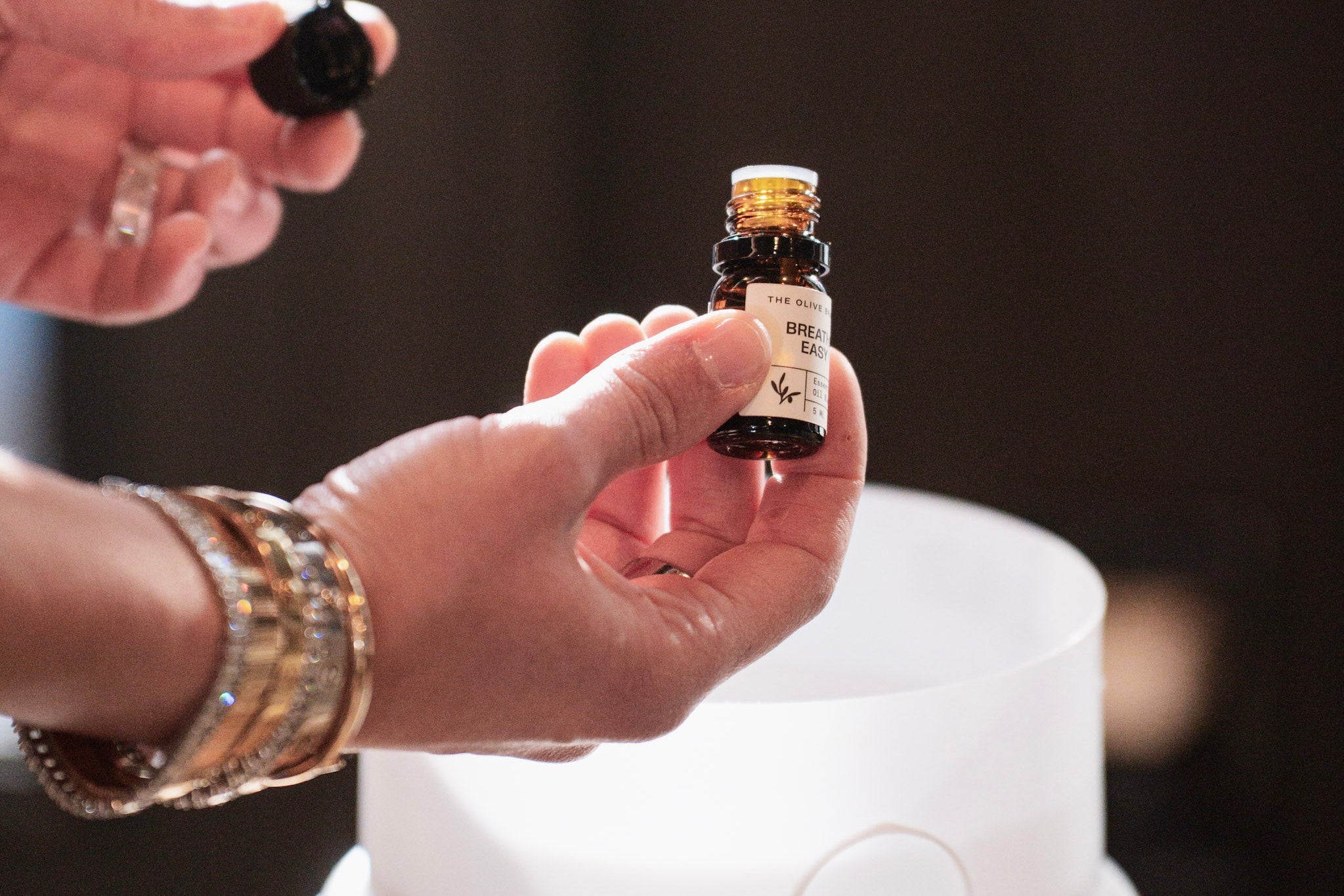 Person holding a small bottle of essential oil above an ultrasonic humidifier.