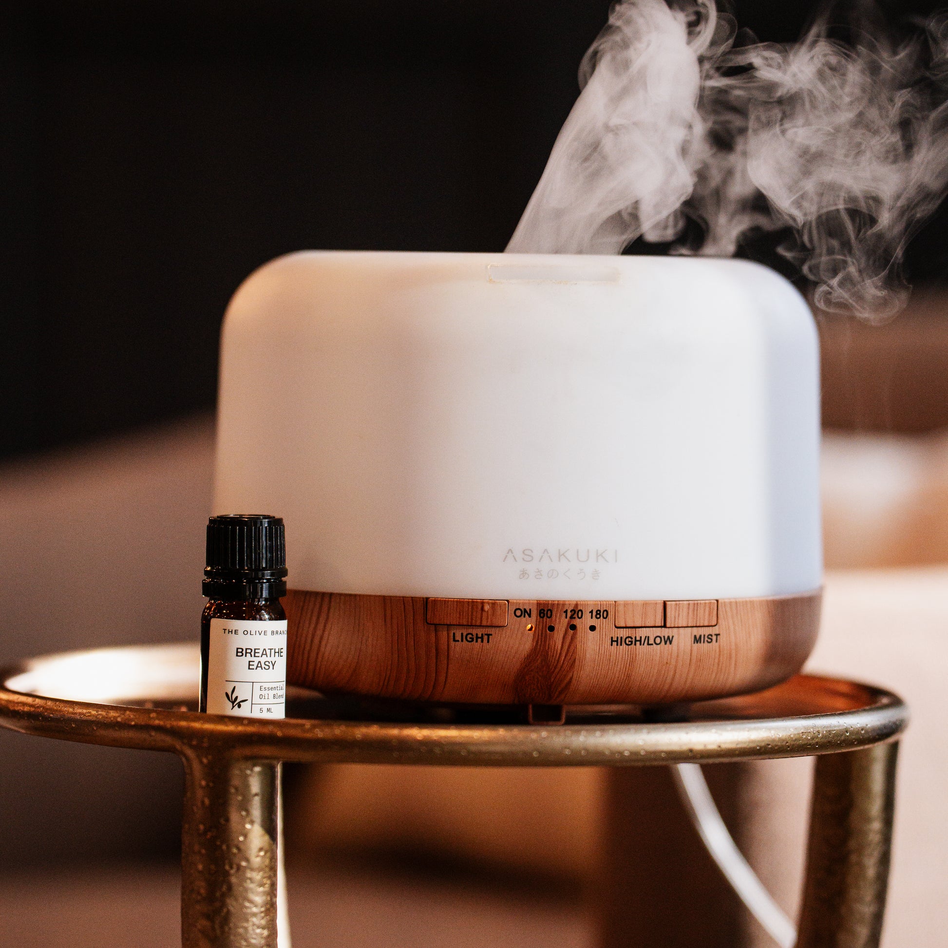 Aromatherapy diffuser with steam and a bottle labeled 'Breathe Easy' on a wooden stand.