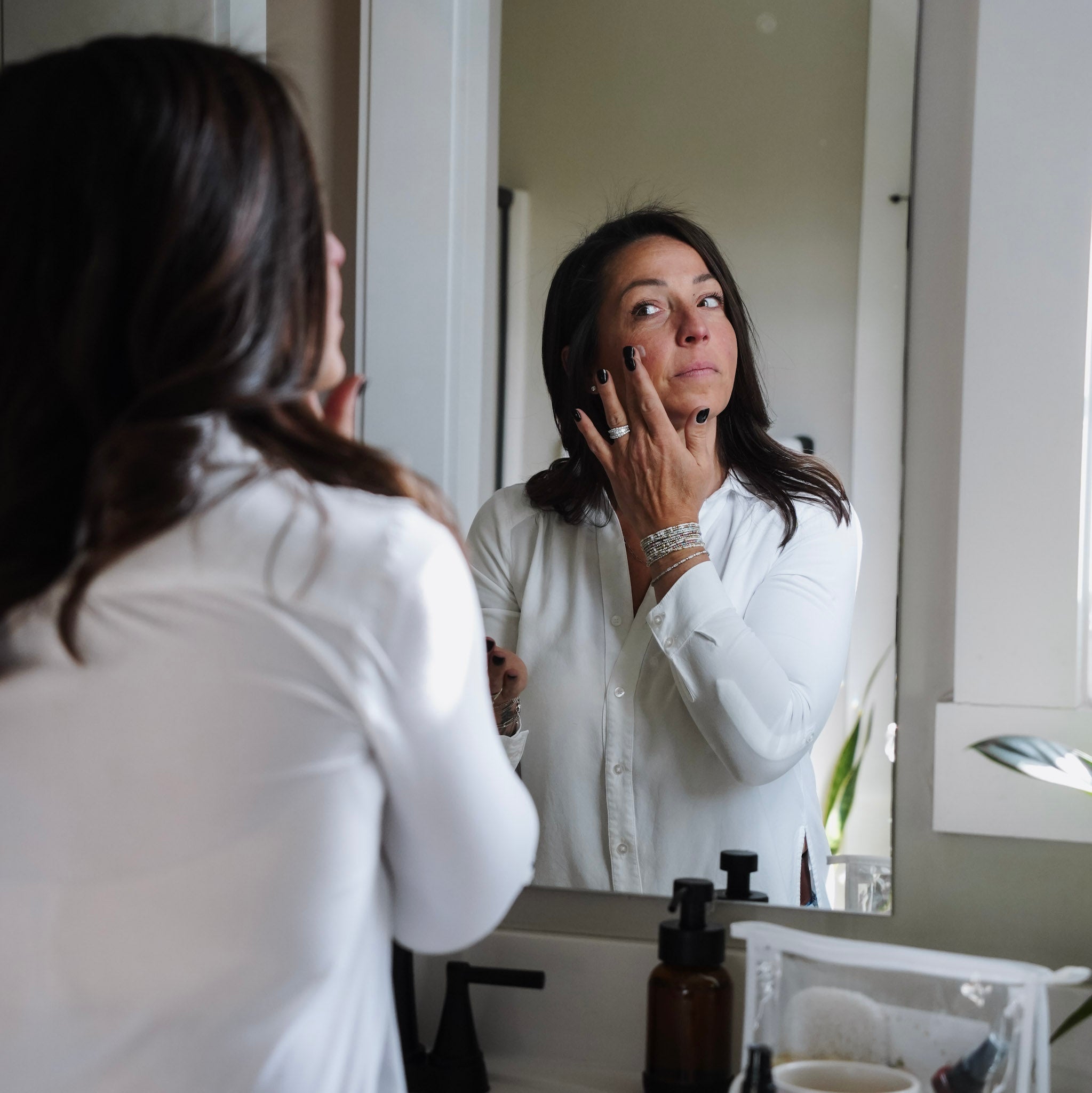 Woman applying calendula serum in front of a mirror