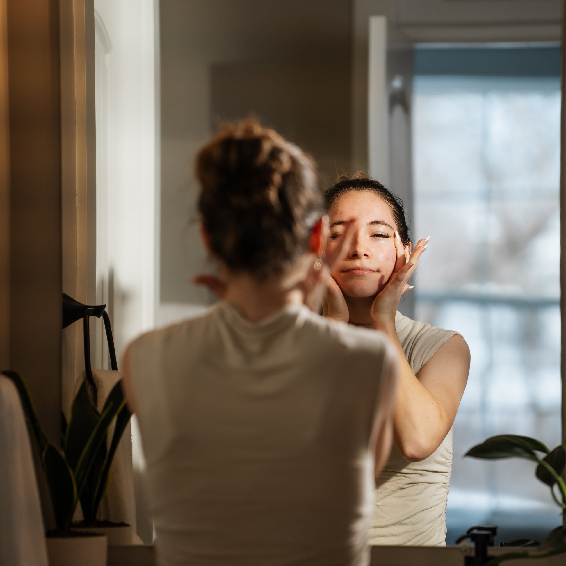Woman applying calendula serum product in front of a mirror in a bathroom.