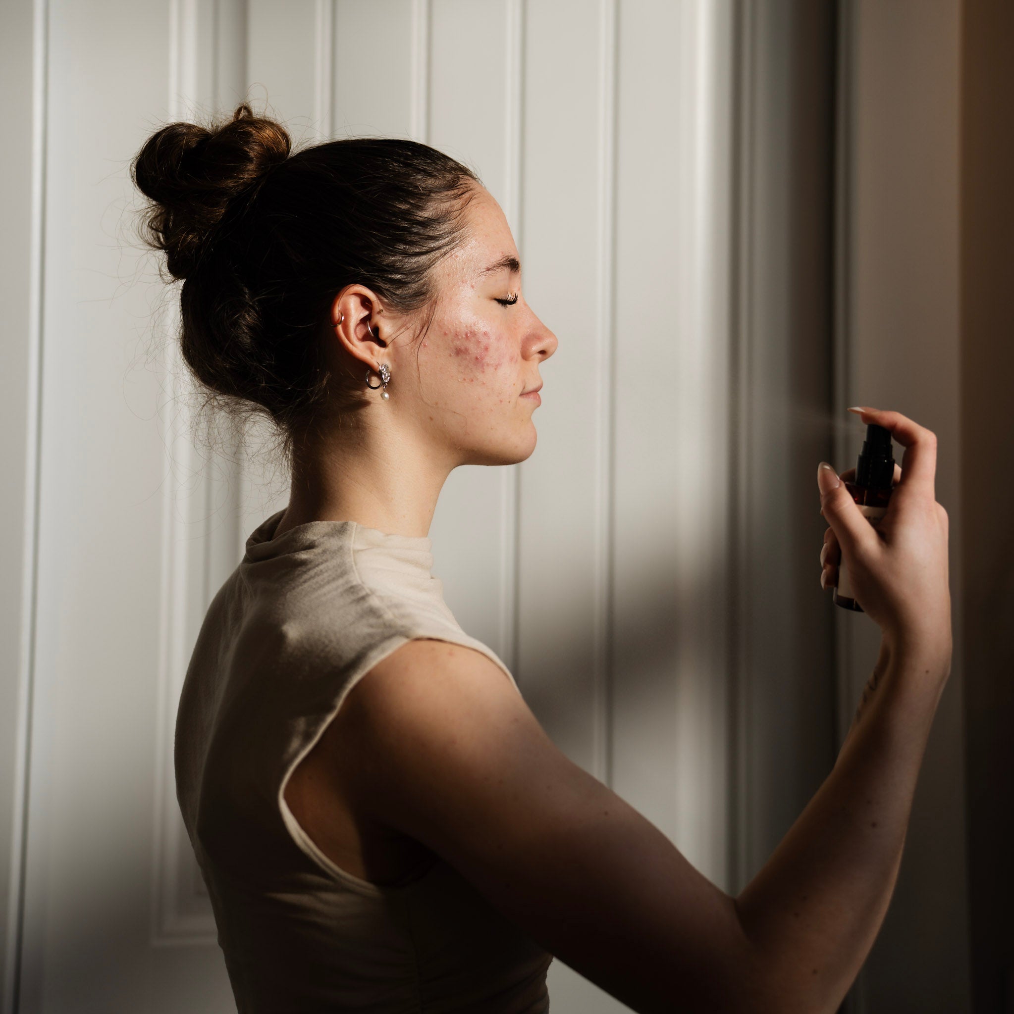 Woman applying balancing calendula toner to her face with a neutral background.