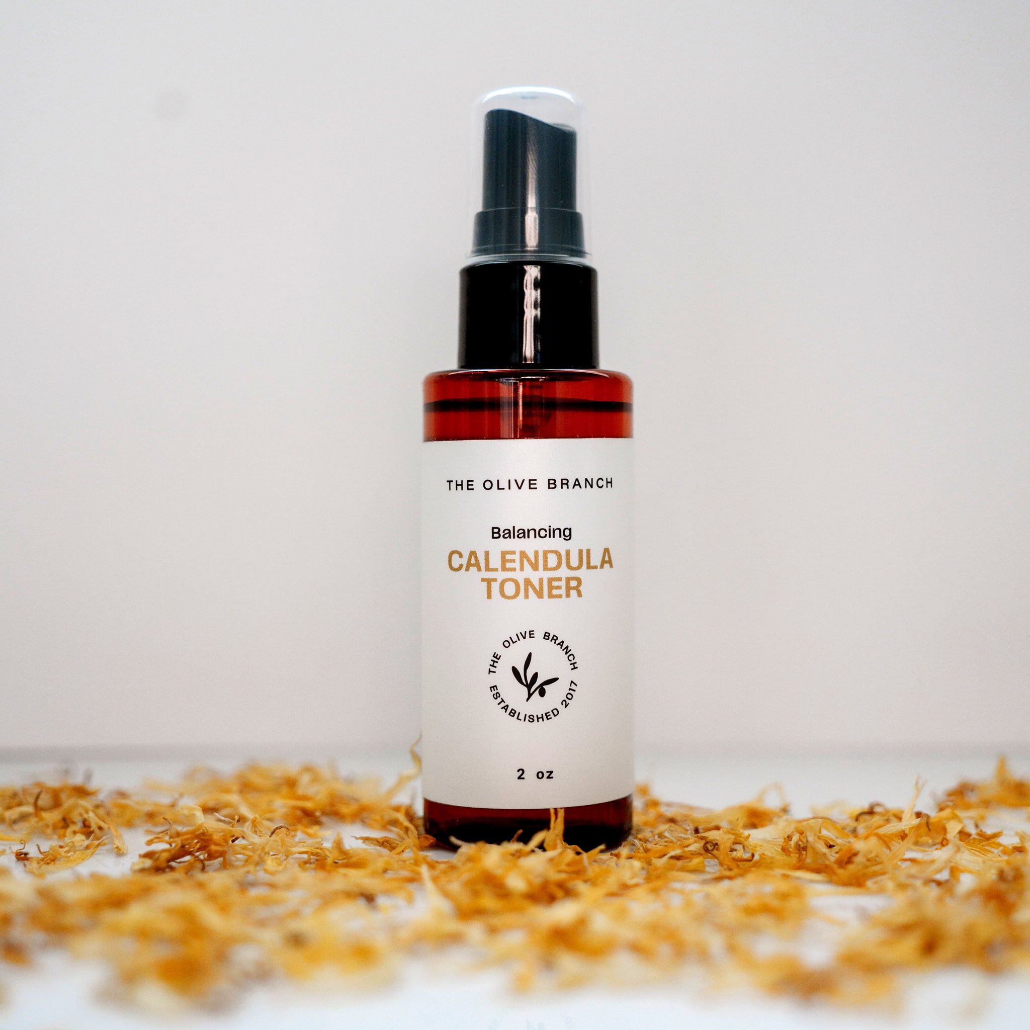 Bottle of The Olive Branch Calendula Toner on a white background with dried flowers.