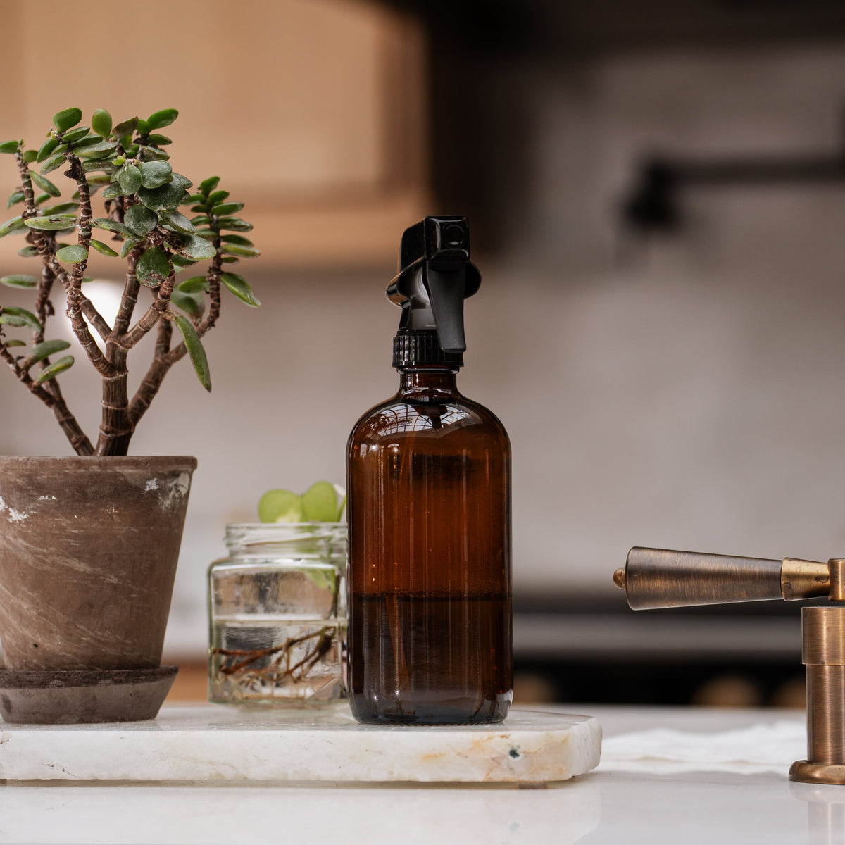 Brown glass bottle with black spray nozzle on a marble surface with decorative items.