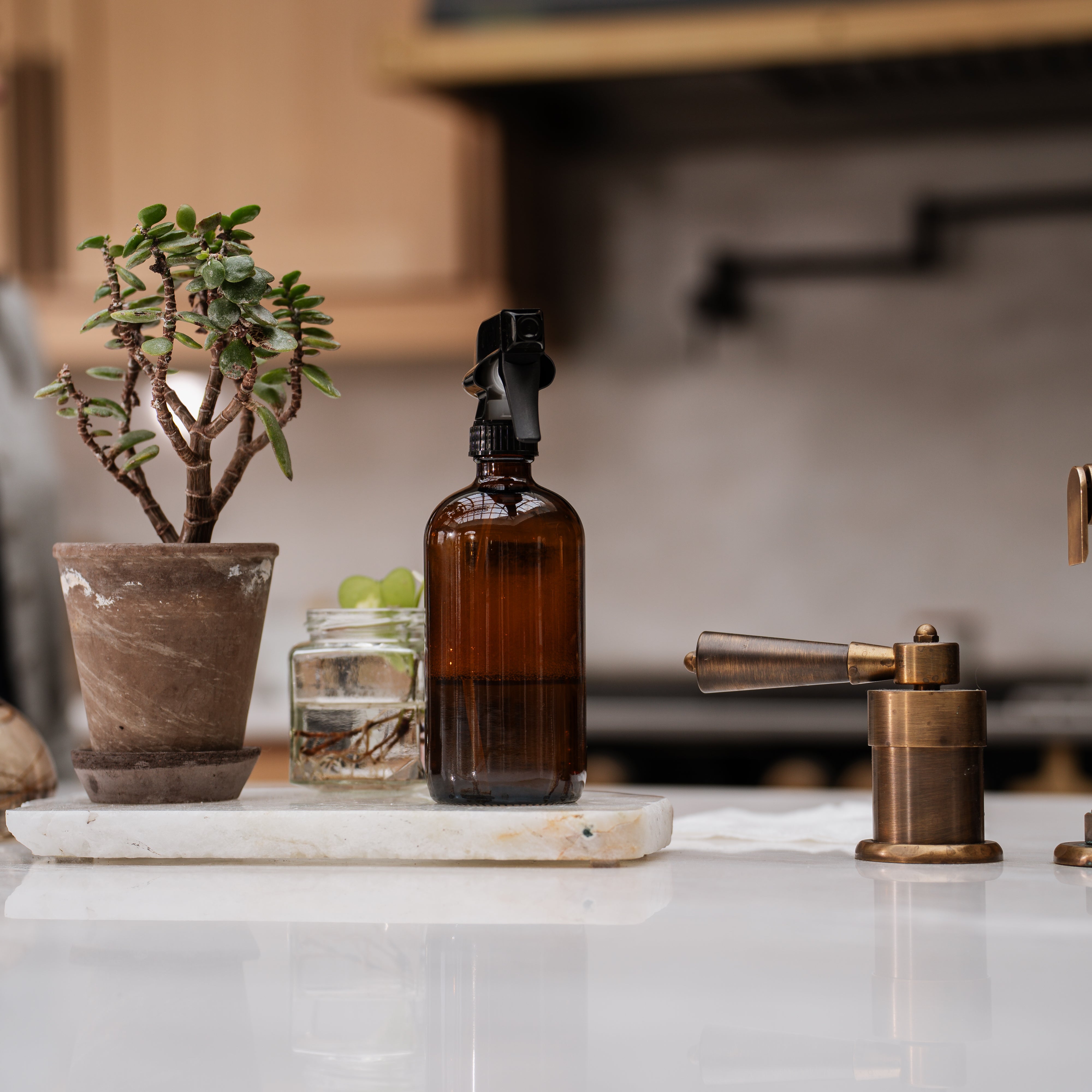 Brown glass bottle with black spray nozzle on a marble surface with decorative items.
