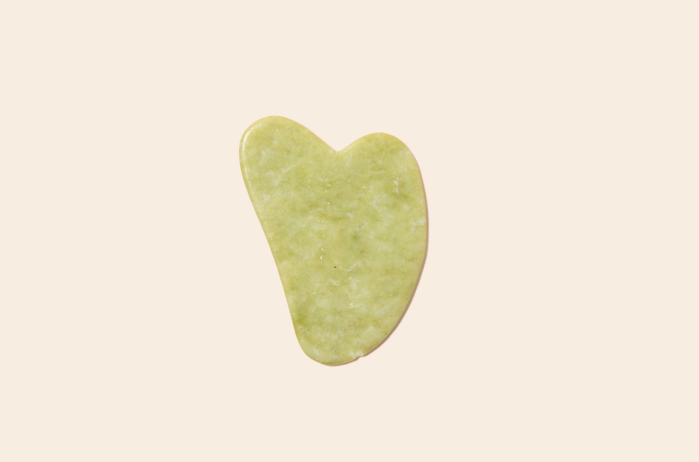 Green jade gua sha on a plain background.