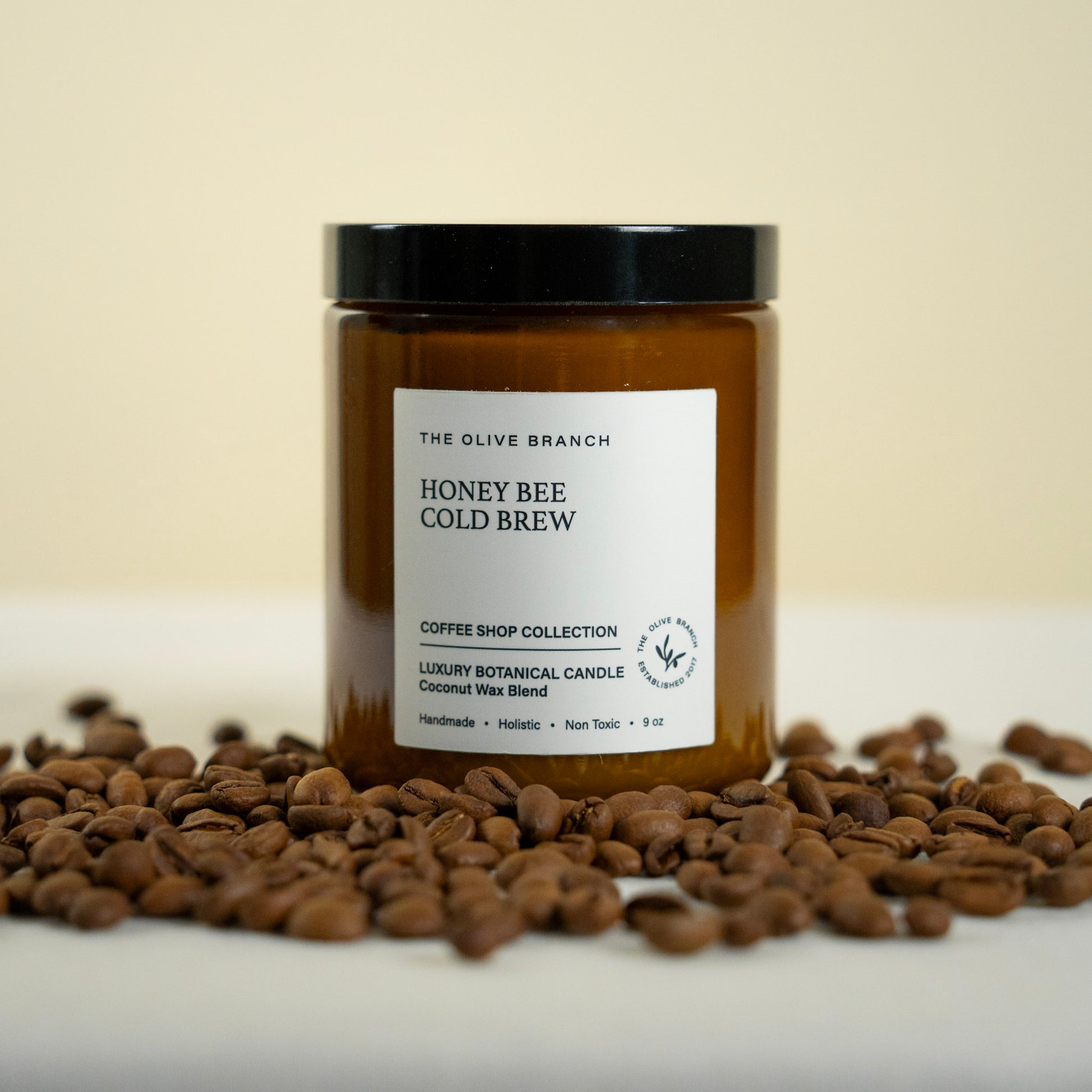 Jar of 'Honey Bee Cold Brew' candle from The Olive Branch on a surface with coffee beans.