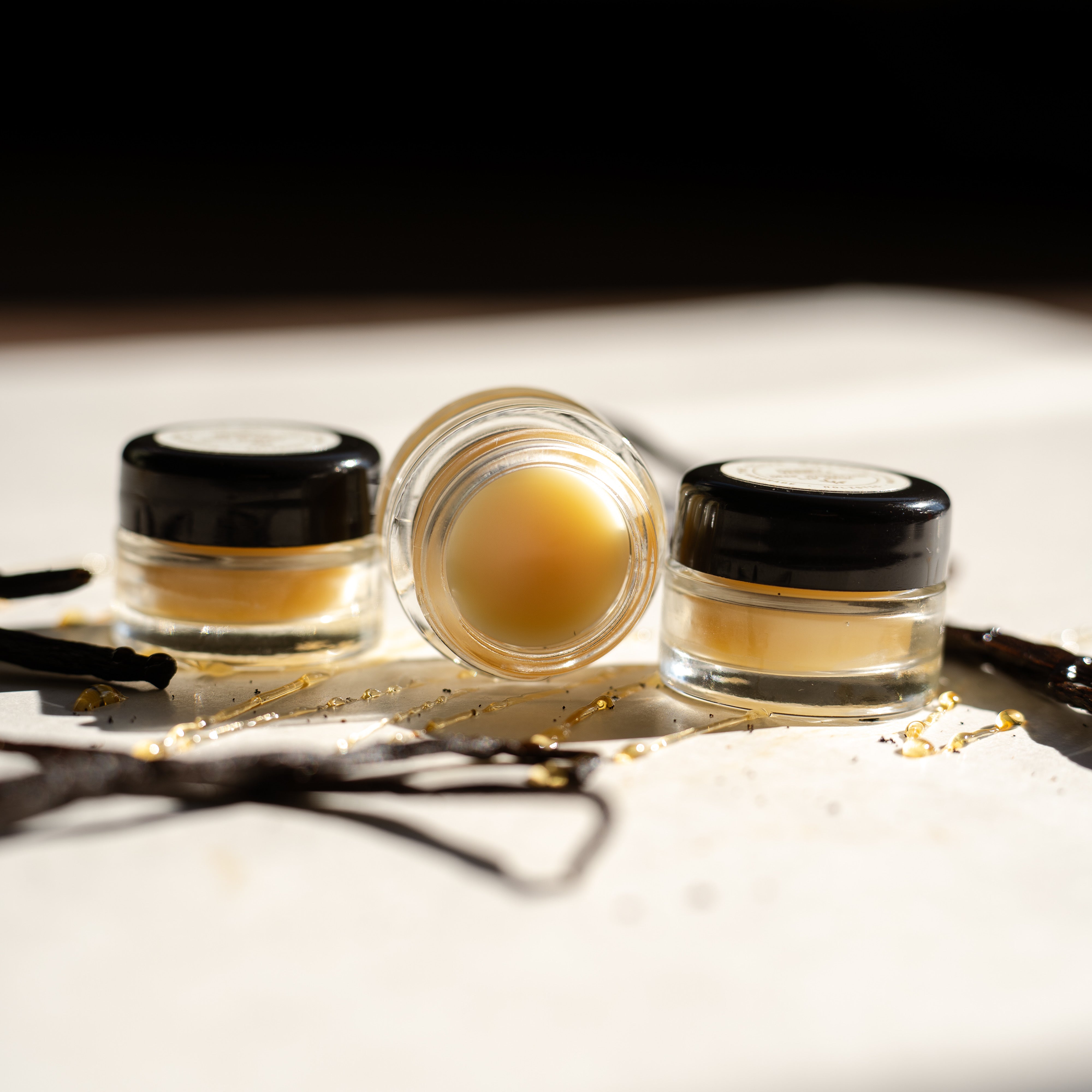 Three small glass jars with black lids containing lip mask on a white surface.