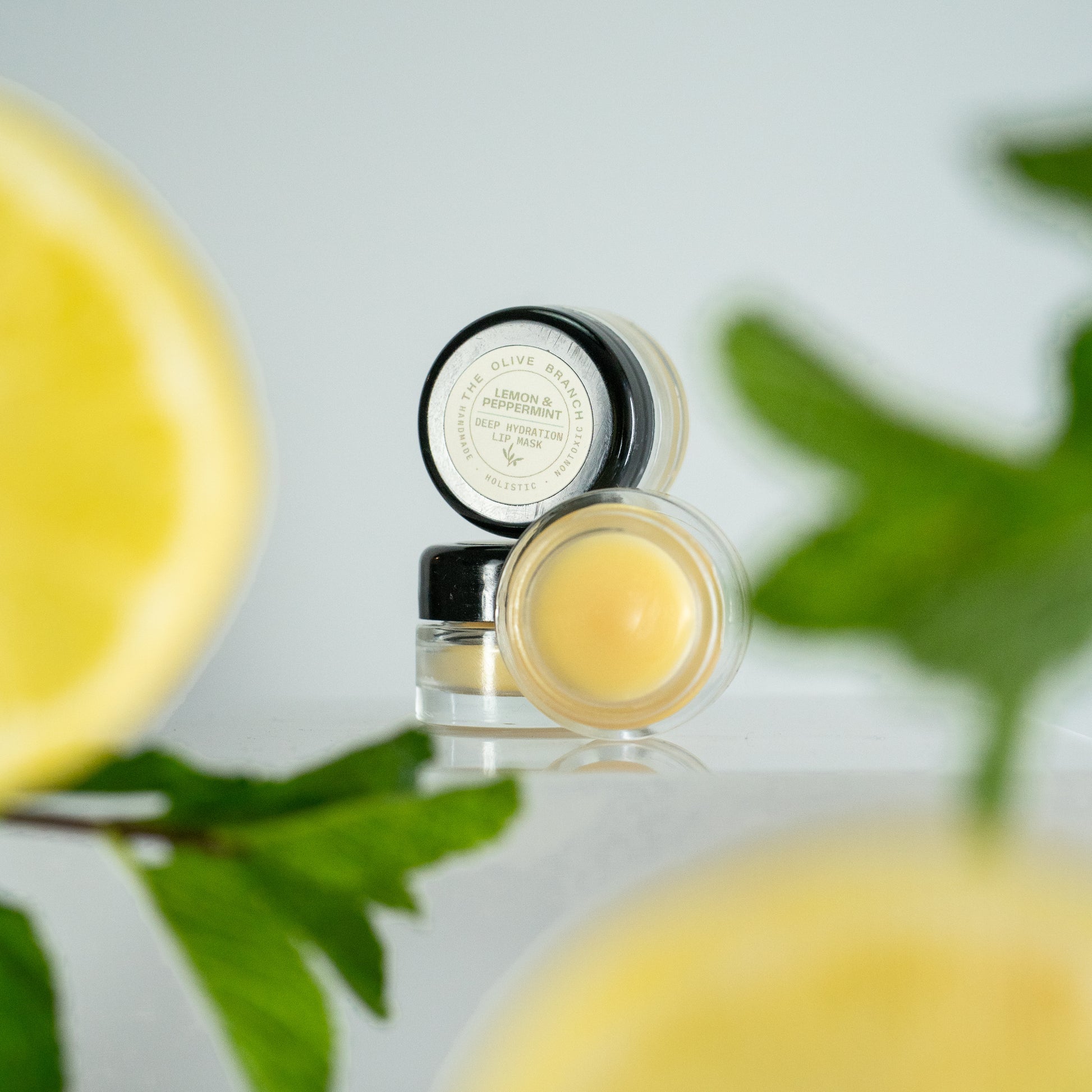 Two small jars of lip balm with a lemon and green leaves in the background