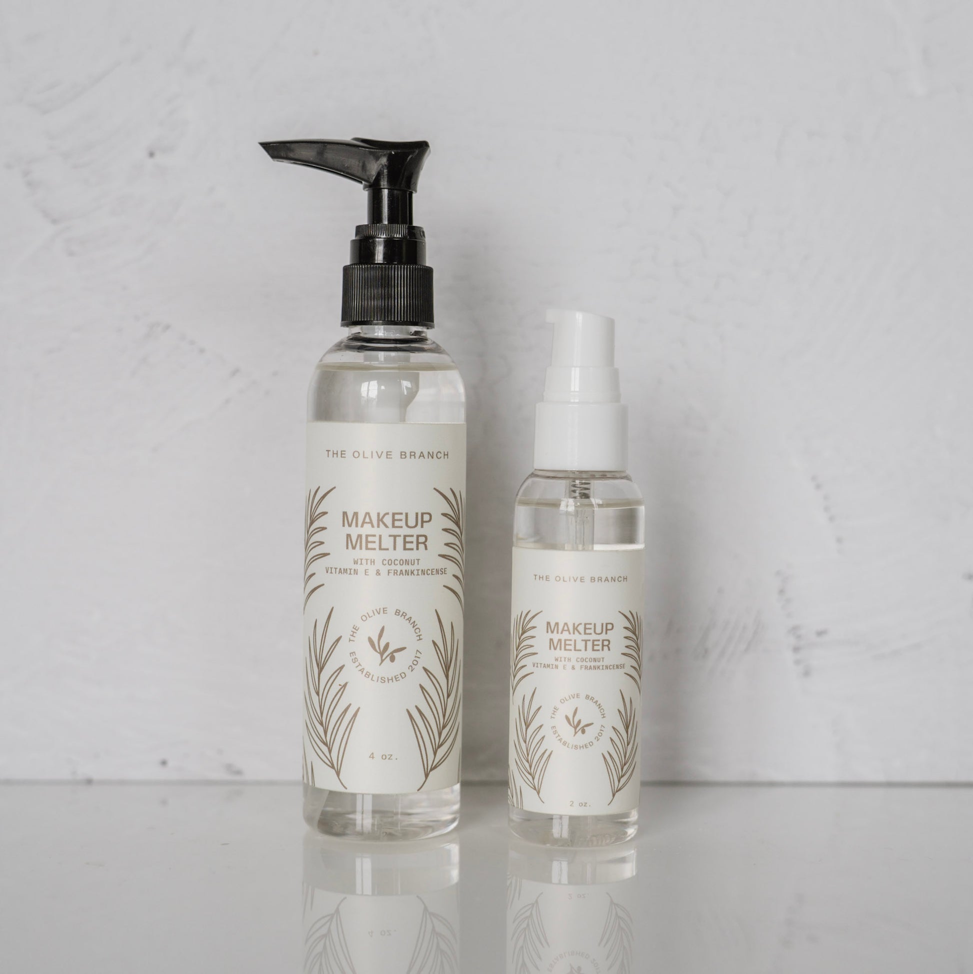 Two bottles of 'Makeup Melter' by The Olive Branch on a light gray background