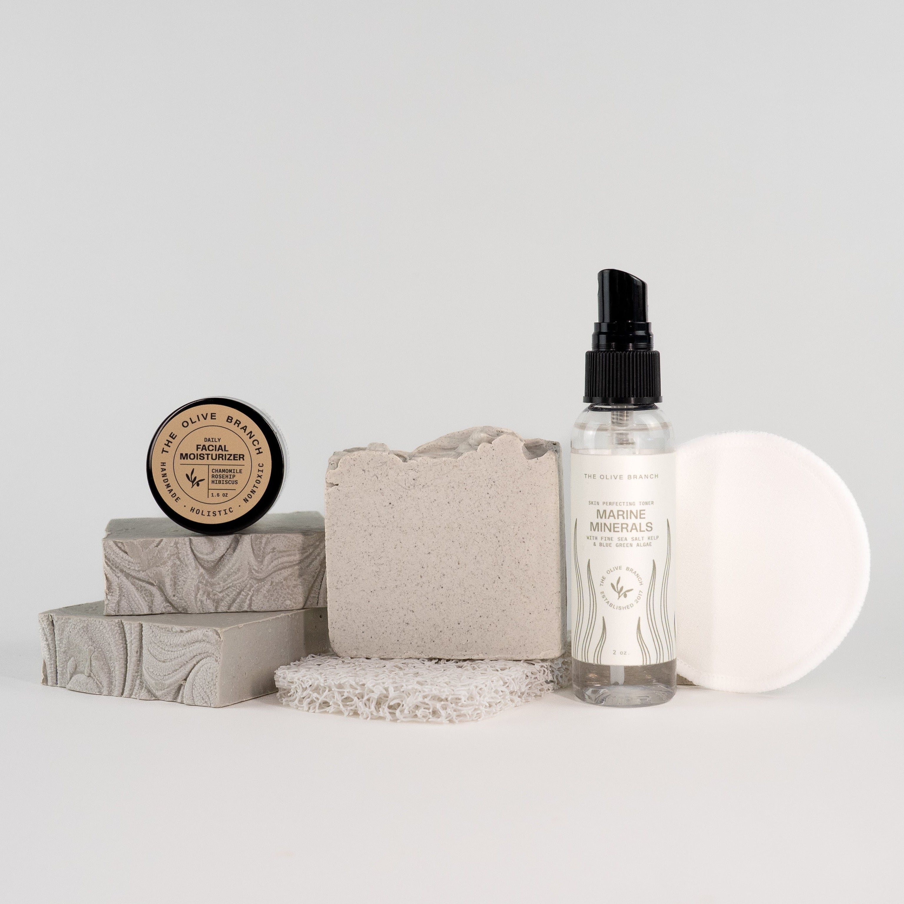 Collection of skincare products including a bottle, soap, and cream on a light gray background
