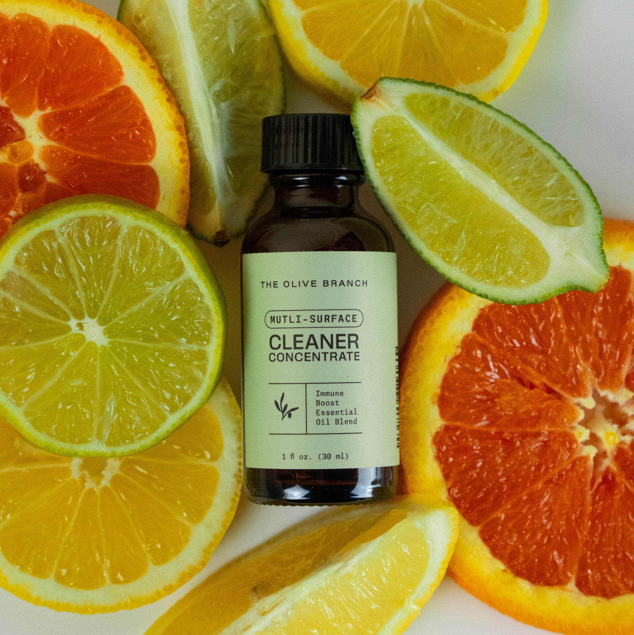 Bottle of 'The Olive Branch' cleaner concentrate surrounded by sliced citrus fruits on a white background