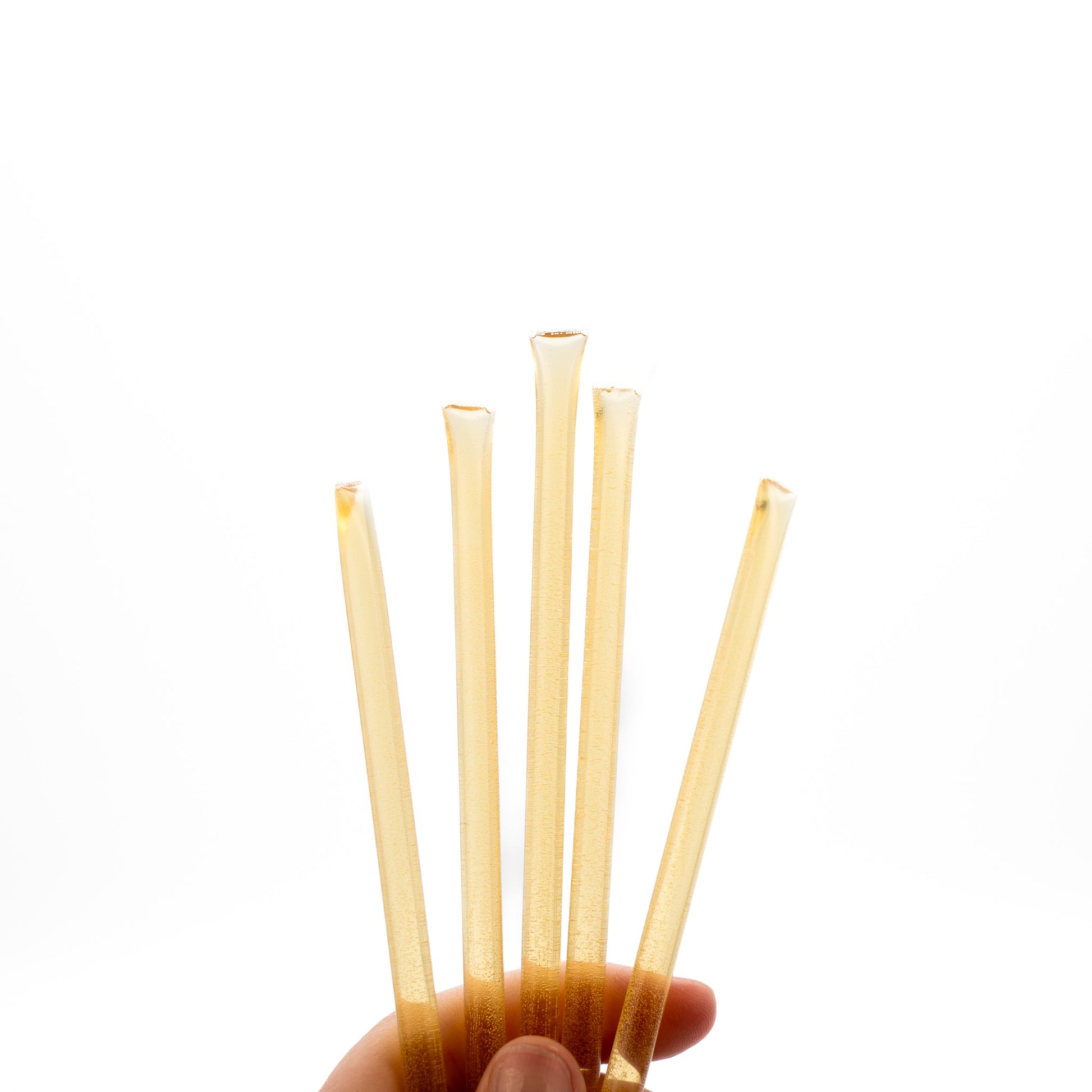 Hand holding five raw honey sticks on a white background.