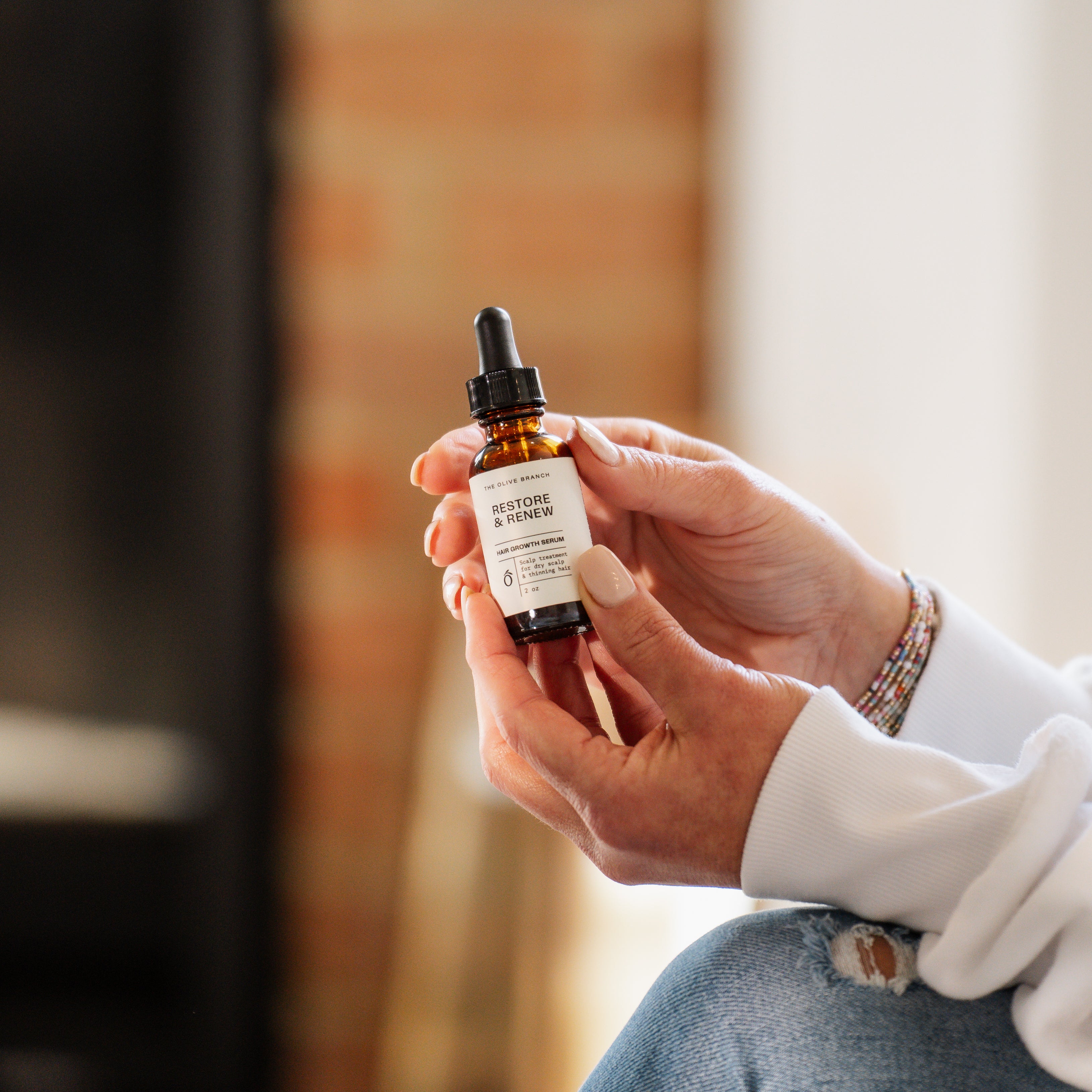 Hand holding a bottle labeled 'Restore & Renew' against a blurred indoor background