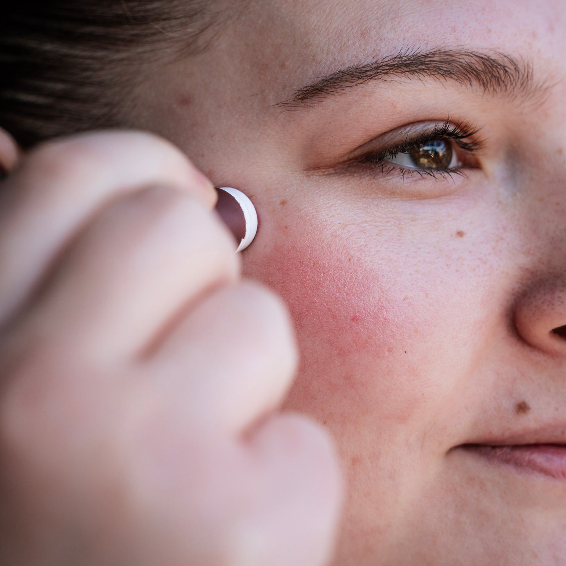 Person applying rose gold tinted lip balm to her cheek.