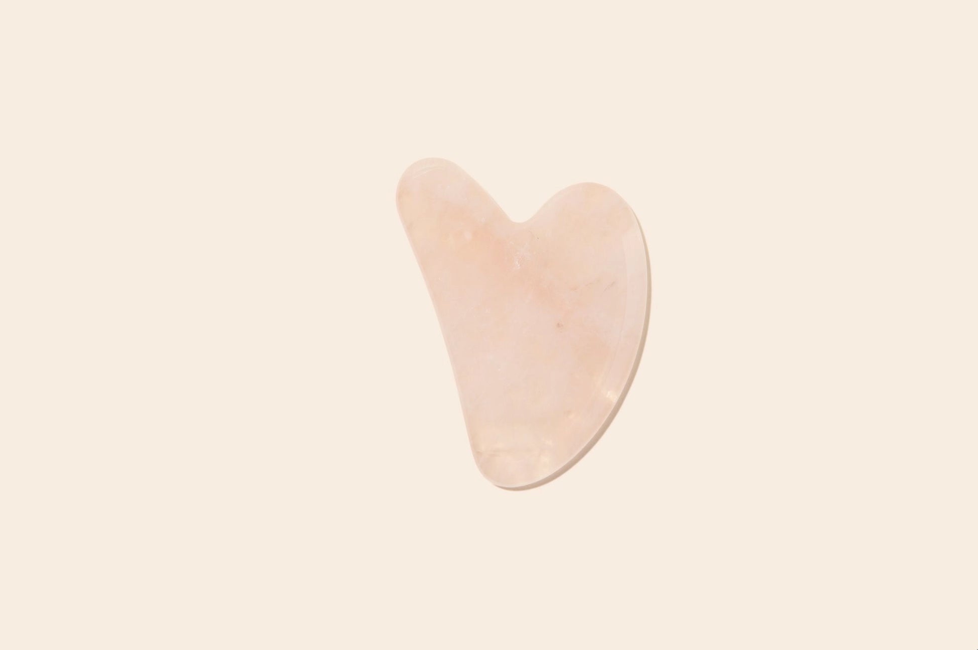 Rose quartz gua sha on a plain background