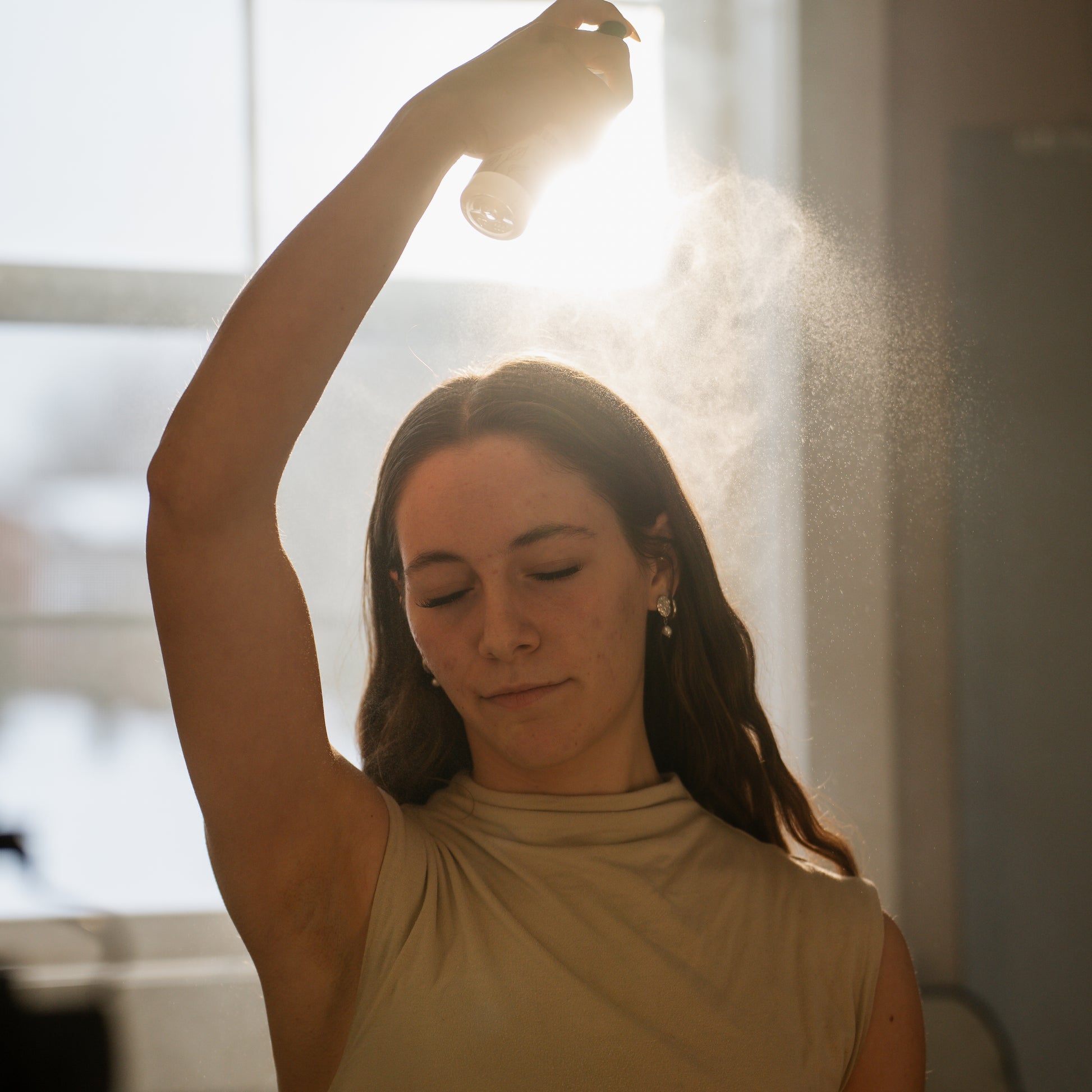 Woman holding a bottle of Rose Water Mist in front of a mirror with a blurred background