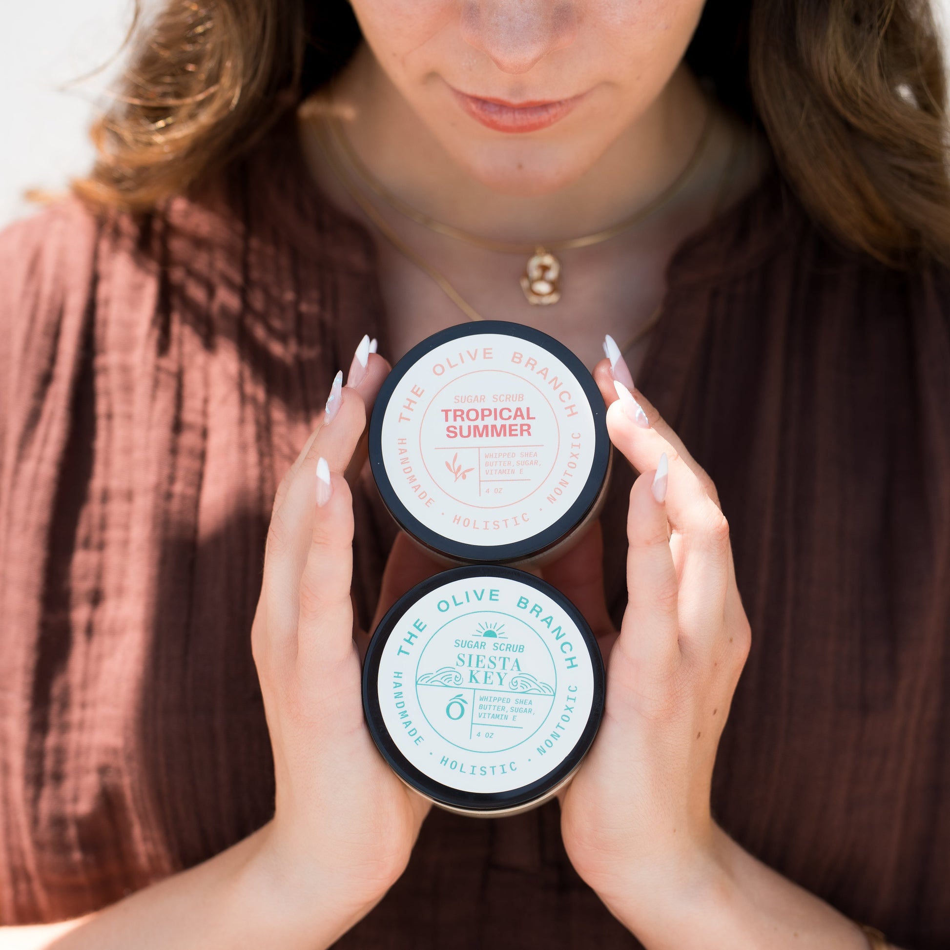 Woman holding two jars of a sugar scrubs with a neutral background