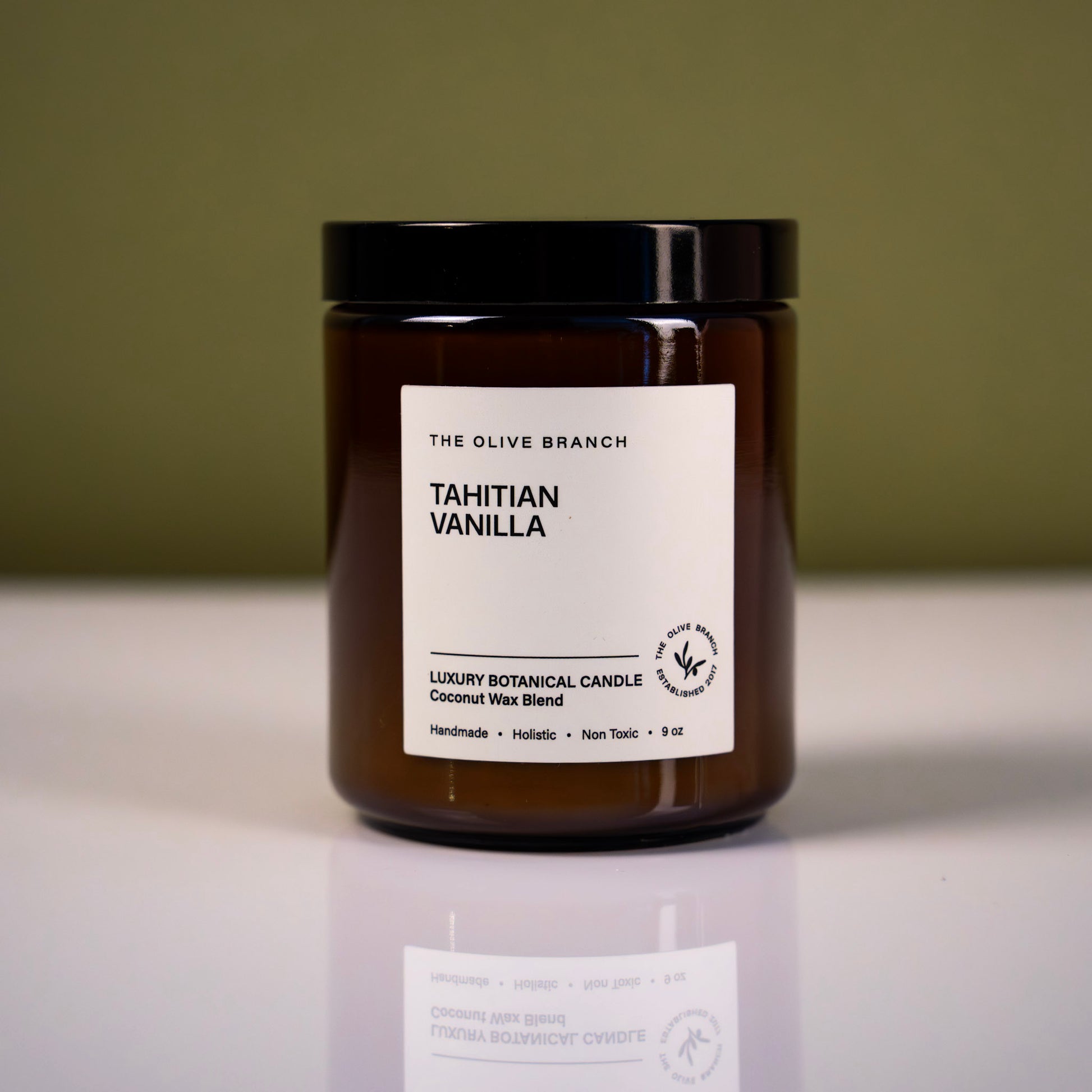 Brown candle jar labeled 'Tahitian vanilla' with a label on a reflective surface and green background