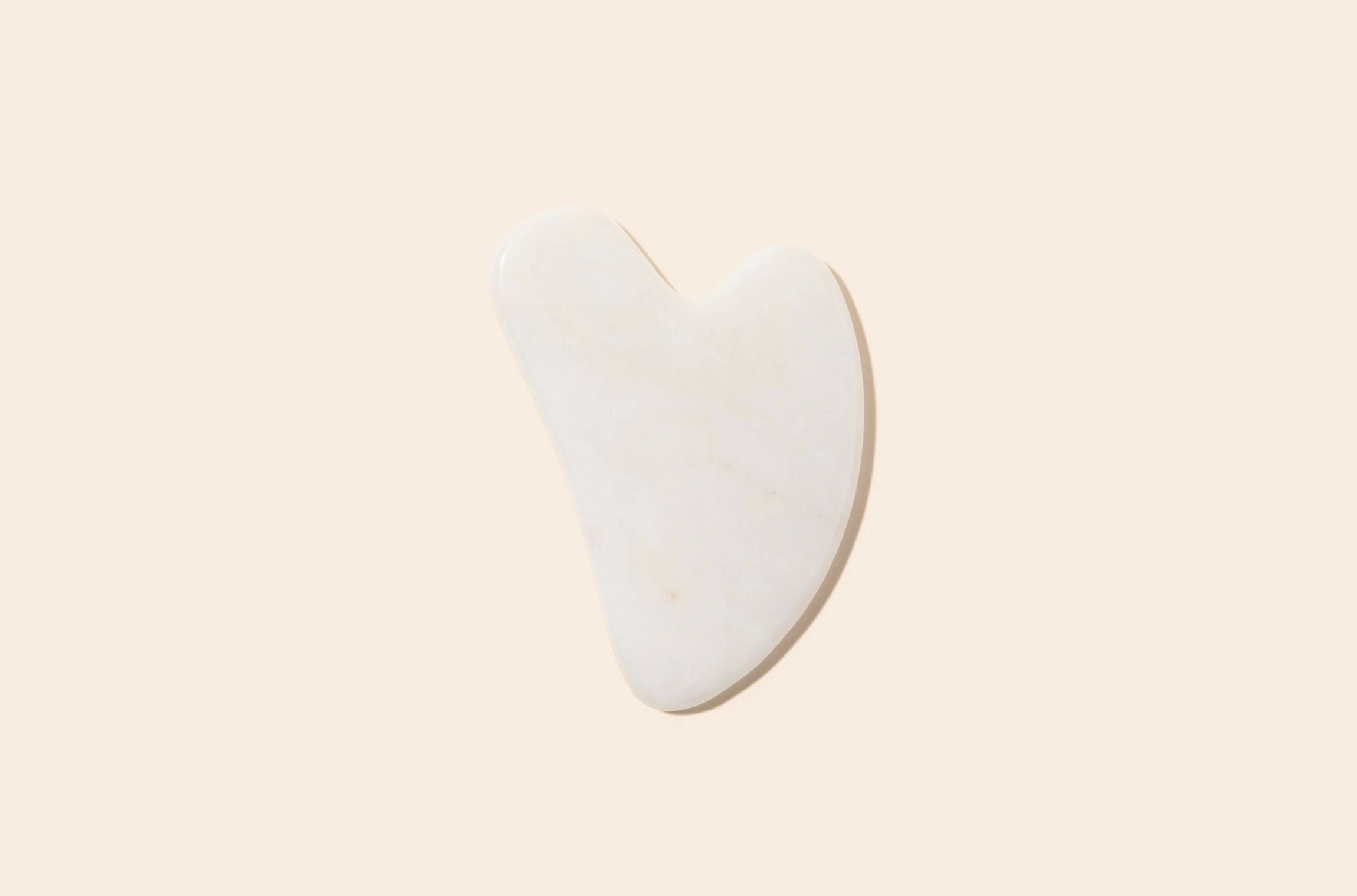 White jade gua sha on a plain background.