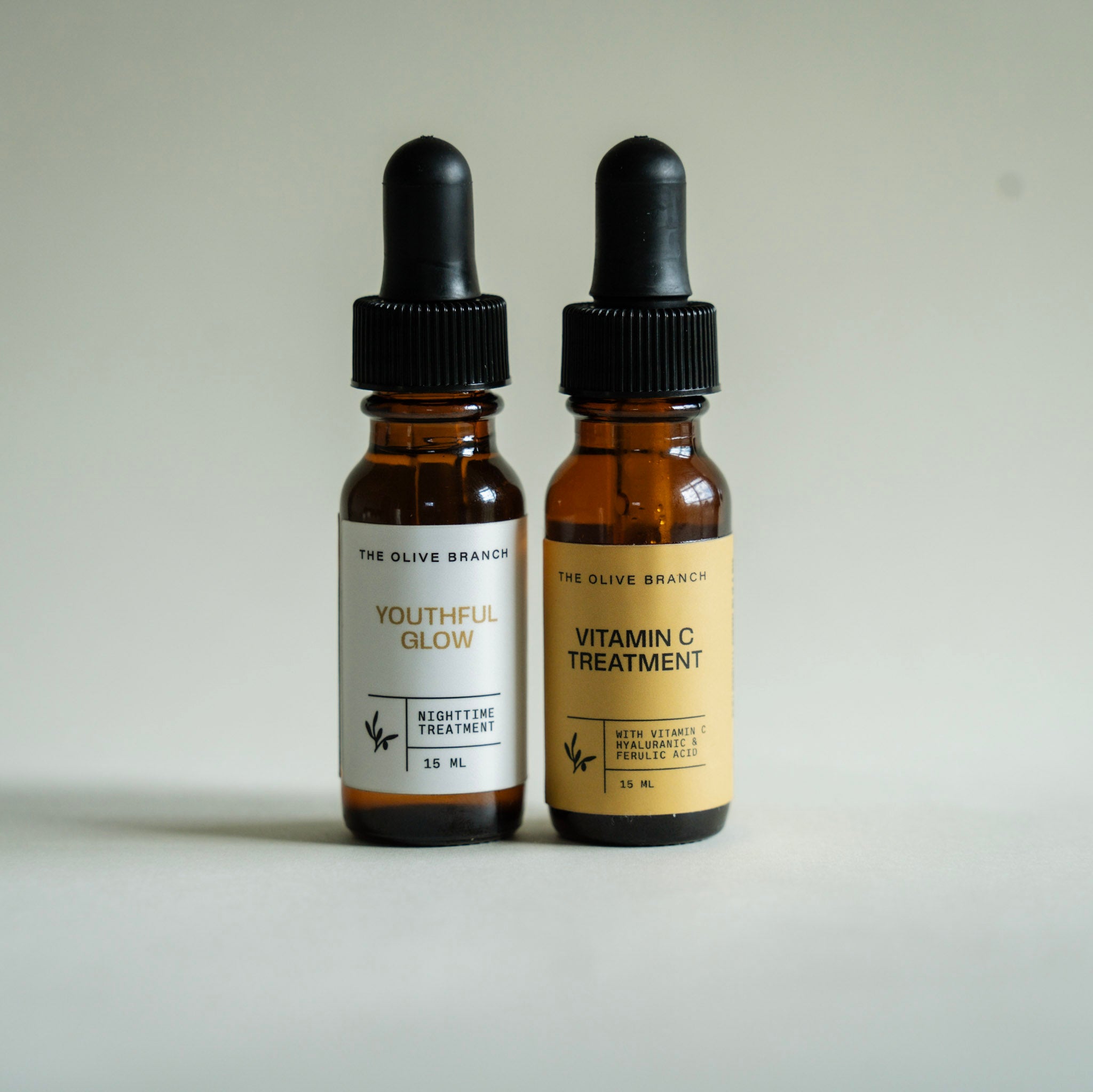 Two bottles of skincare treatments from The Olive Branch on a neutral background